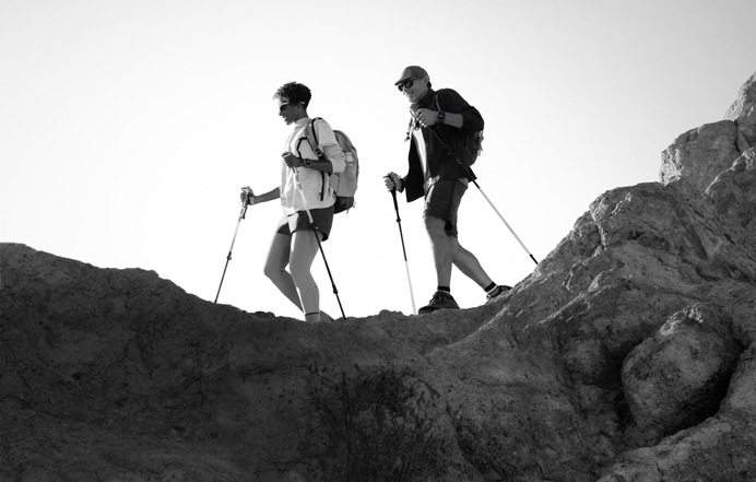 Two people wearing Apple Watch devices and hiking on a rocky trail with poles and gear