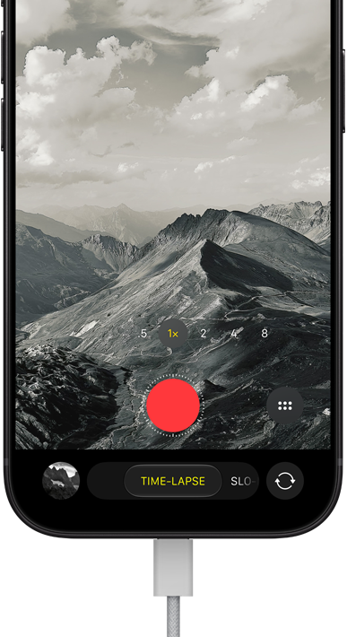 iPhone 18 Pro, front exterior, displaying a mountainous landscape, with the camera mode overlay in Time-Lapse mode, with power cable attached to charging port