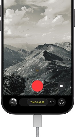 iPhone 18 Pro, front exterior, displaying a mountainous landscape, with the camera mode overlay in Time-Lapse mode, with power cable attached to charging port