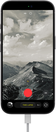 iPhone 18 Pro, front exterior, displaying a mountainous landscape, with the camera mode overlay in Time-Lapse mode, with power cable attached to charging port