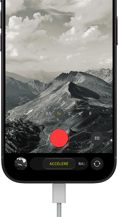 Un iPhone 18 Pro, face avant, affichant un paysage montagneux, avec le menu superposé du mode caméra en mode accéléré, câble d’alimentation branché au port de recharge