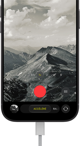 Un iPhone 18 Pro, face avant, affichant un paysage montagneux, avec le menu superposé du mode caméra en mode accéléré, câble d’alimentation branché au port de recharge