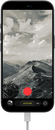 Un iPhone 18 Pro, face avant, affichant un paysage montagneux, avec le menu superposé du mode caméra en mode accéléré, câble d’alimentation branché au port de recharge