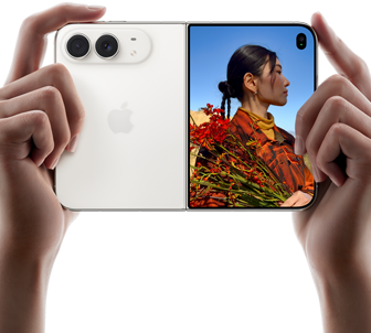 iPhone Duo, couleur blanc stellaire, deux mains le tiennent en orientation horizontale, déplié, le volet gauche montre les deux caméras arrière Fusion 48 mégapixels, le volet droit montre l’écran externe affichant une personne en train de se faire photographier, qui peut se voir pendant la prise grâce à Duo Preview